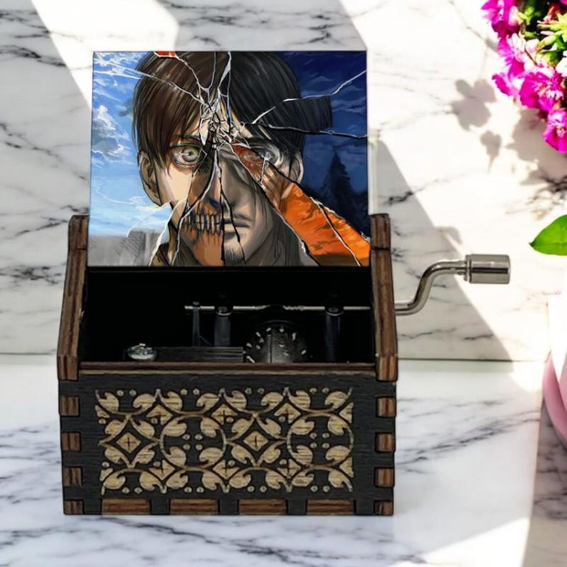 May include: A wooden music box with a hand-crank on the side. The lid features a colorful image of a character from the anime Attack on Titan. The box has a decorative design on the front.