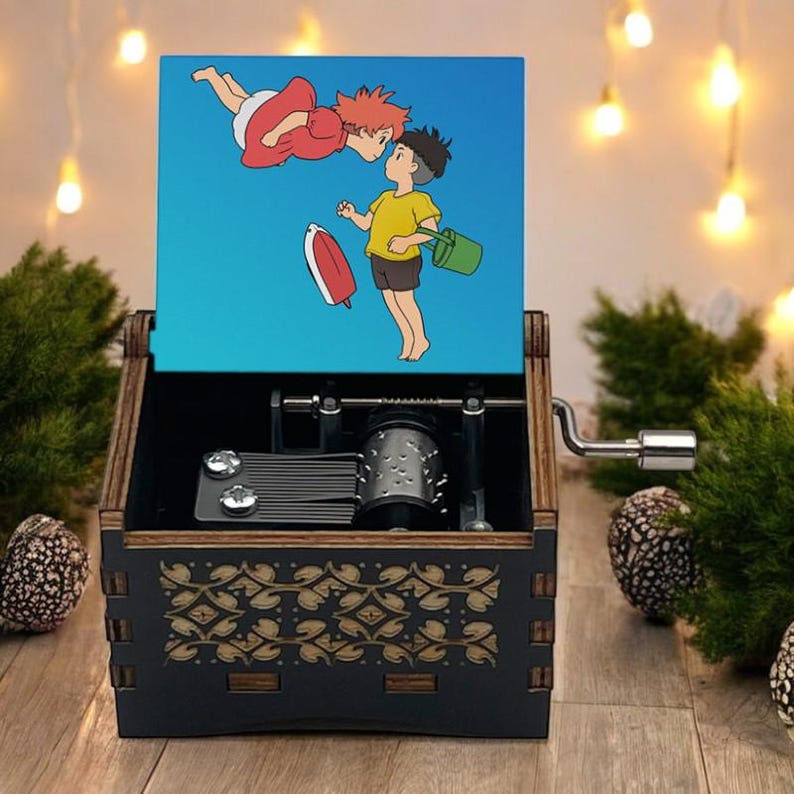 Pode incluir: Uma caixa de m&uacute;sica de madeira com uma manivela no lado. A tampa da caixa apresenta uma ilustra&ccedil;&atilde;o colorida de dois personagens de anime, uma menina com cabelo vermelho e um menino com cabelo castanho, flutuando no ar. A caixa tem um design decorativo na frente.