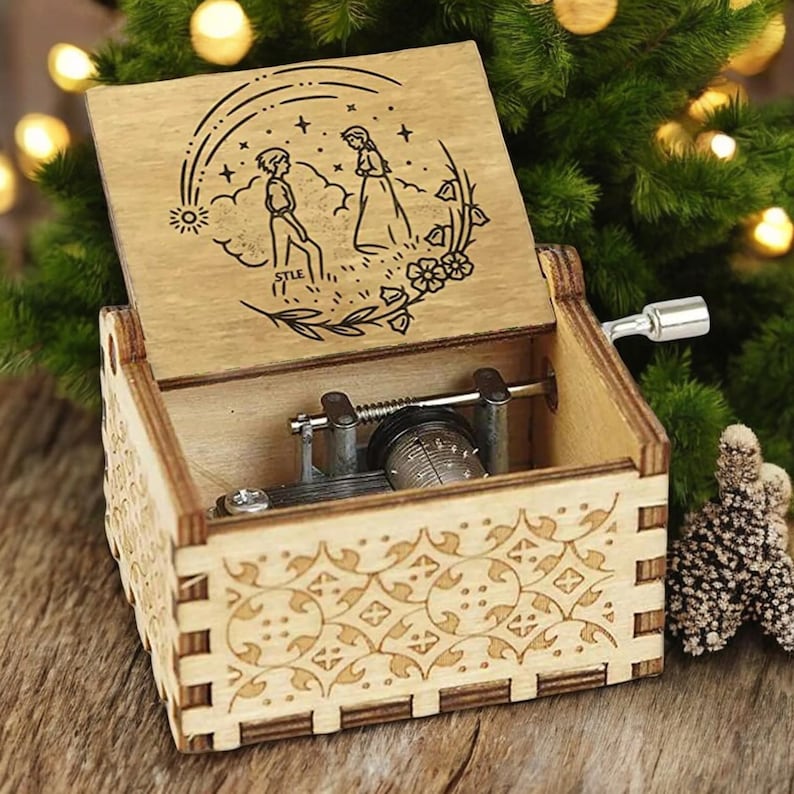 May include: Wooden music box with a hand-crank mechanism. The lid features a laser-engraved design of a couple walking under a rainbow with stars and flowers. The box has a decorative pattern on the sides.