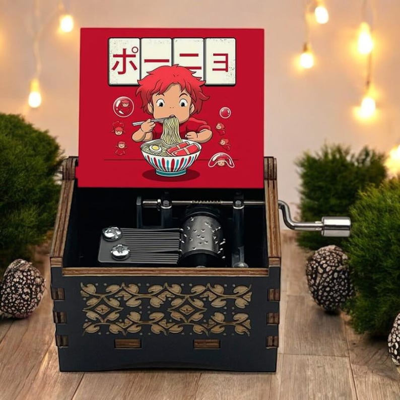 Pode incluir: Uma caixa de m&uacute;sica de madeira preta com uma tampa vermelha que apresenta um personagem de desenho animado comendo ramen. A tampa tem o texto japon&ecirc;s "ホ-三-目" nela.