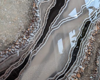 May include: Abstract art painting with black and silver lines and glitter, resembling an agate geode. The background is white with a textured, glittery surface.