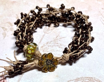 May include: A brown and beige beaded bracelet with a green glass bead and a gold flower charm.