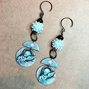 May include: A pair of dangle earrings with a blue and white angel charm and a blue and white polka dot bead.