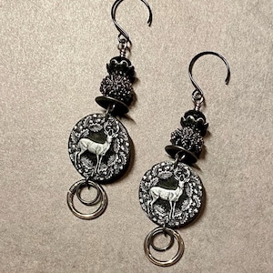 May include: A pair of dangle earrings with a black and silver deer charm, black beads, and silver hoops.