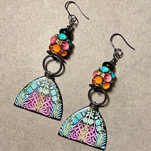 May include: A pair of dangle earrings with a black metal wire and a cluster of colorful glass beads. The bottom of the earrings feature a black metal arch with a floral design in shades of pink, blue, and green.