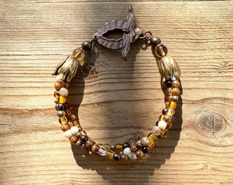 May include: A multi-strand bracelet with brown, gold, and white beads. The bracelet has a unique clasp with a leaf design.