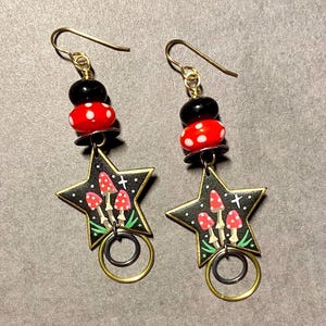 May include: A pair of gold star-shaped earrings with black and white polka dot beads, red and white mushroom designs, and gold and silver rings.