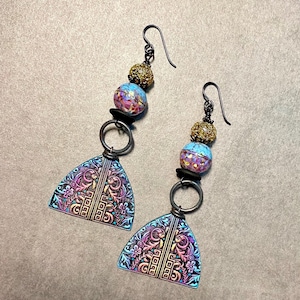 May include: A pair of dangle earrings with a blue, pink, and gold patterned bead, a gold ring, and a triangular pendant with a floral design. The pendant is a deep blue with pink and gold accents.