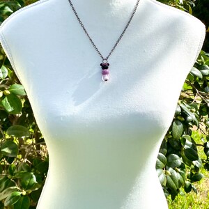 May include: A silver chain necklace with a pendant featuring three beads. The top bead is black, the middle bead is purple, and the bottom bead is white.