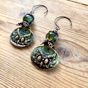 May include: A pair of green and gold owl earrings with black wire hooks and green and gold glass beads.
