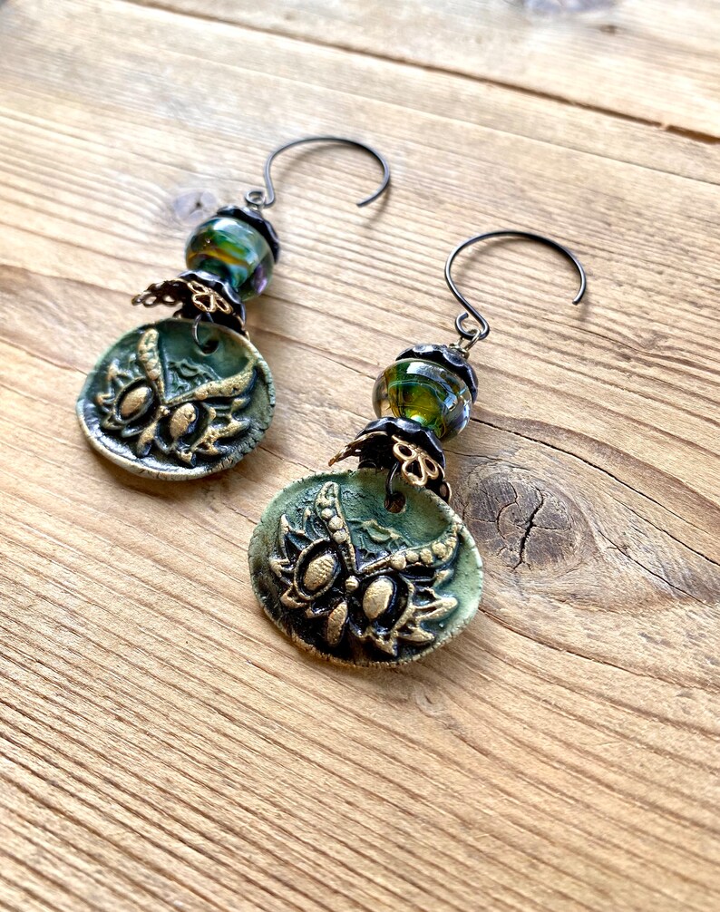 May include: A pair of green and gold owl earrings with black wire hooks and green and gold glass beads.