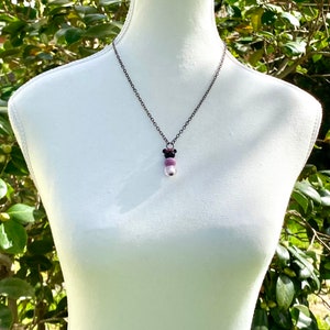 May include: A silver chain necklace with a pendant made of three round beads. The beads are purple, pink, and white.
