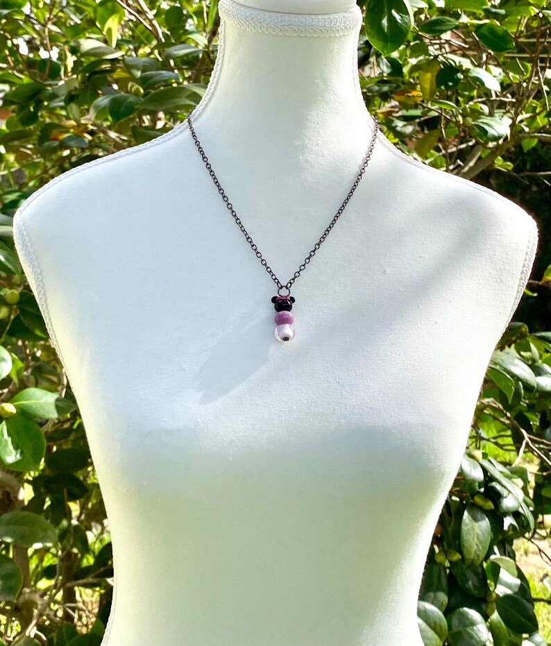 May include: A silver chain necklace with a pendant made of three round beads. The beads are purple, pink, and white.