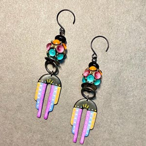 May include: A pair of dangle earrings with a black, yellow, orange, pink, and turquoise bead cluster at the top and a black, yellow, and pink painted design on the bottom.