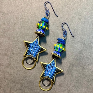 May include: A pair of dangle earrings with blue and yellow star-shaped charms and blue and green glass beads. The earrings have gold-colored hoops and blue wire hooks.