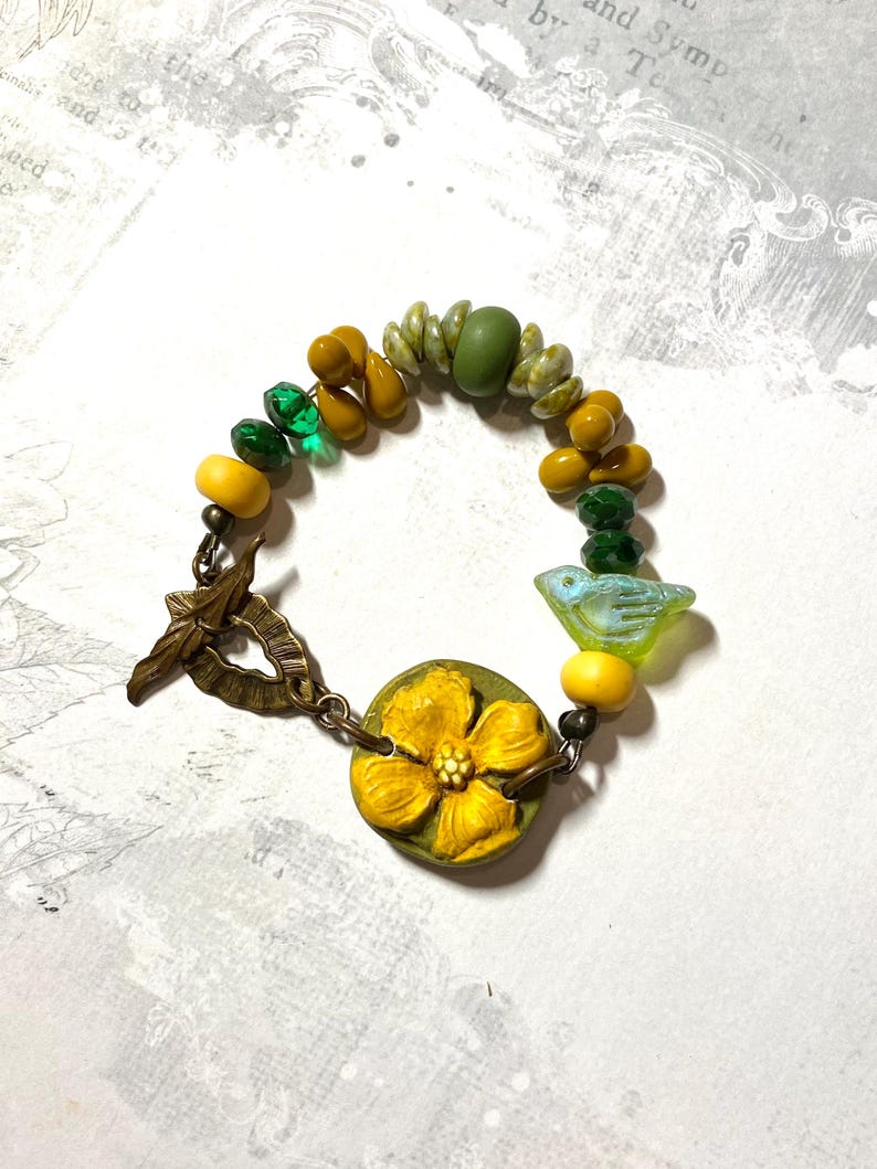 Puede incluir: Una pulsera artesanal con un dije de flor amarilla y una cuenta en forma de p&aacute;jaro. La pulsera incorpora cuentas amarillas, verdes y transparentes, conectadas por un cierre de tono bronce. La longitud de la pulsera es de aproximadamente 18 cm.