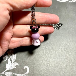 May include: A black and purple beaded necklace with a black and pink Minnie Mouse charm. The necklace is on a black chain.