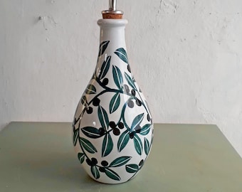 May include: White ceramic olive oil bottle with a green and black olive branch design. The bottle has a silver pour spout.