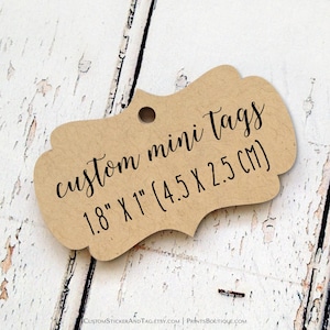 May include: A tan, scalloped-edge paper tag with a single hole punch at the top. The tag features black printed text that reads: custom mini tags 1.8" x 1" (4.5 x 2.5 cm). The tag has a textured, fibrous appearance and a curved, decorative shape.