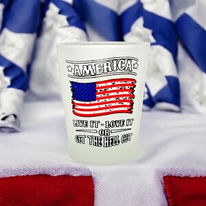 May include: White shot glass with a distressed American flag design and the text "America, Live it - Love it - Or Get the Hell Out".