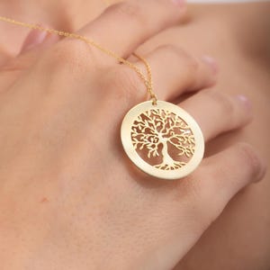 May include: A gold necklace with a round pendant featuring a detailed tree of life design.
