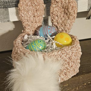 May include: A crocheted bunny basket with a white fluffy tail, filled with colorful Easter eggs and shredded paper.