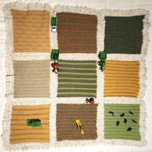 May include: A crocheted baby blanket with a farm theme. The blanket is made of different colored squares, each representing a different part of a farm. There are toy tractors and other farm vehicles on the blanket.