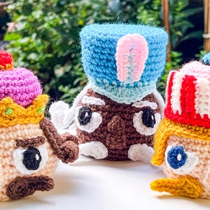 Puede incluir: Tres figuras de crochet con sombreros y rasgos faciales de diferentes colores. La figura de la izquierda tiene un sombrero rosa y amarillo, la figura del medio tiene un sombrero azul y la figura de la derecha tiene un sombrero a rayas rojas y blancas.