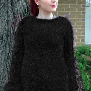 May include: A woman with red hair is wearing a black fuzzy sweater. The sweater has a loose fit and long sleeves.