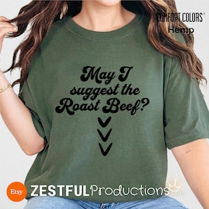 Op de afbeelding: Olijfgroen t-shirt met de tekst "May I suggest the Roast Beef?" in een retro lettertype, met drie pijlen naar beneden. Het shirt heeft de labels Comfort Colors en Hemp.