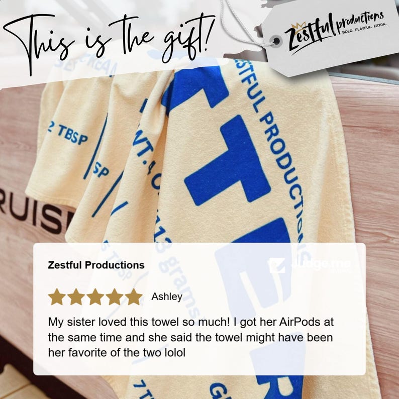 May include: Cream-coloured towel with large blue block letter design and the text "Zestful Productions". The towel also has the text "This is the gift!" in cursive. A customer review is also visible.