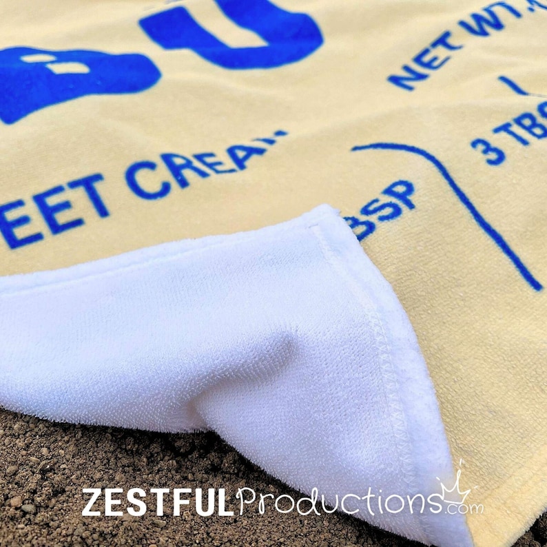 Close-up of butter beach towel corner flipped to show soft white cotton backing, sweet cream design for chefs and bakers, foodie gift towel by Zestful Productions