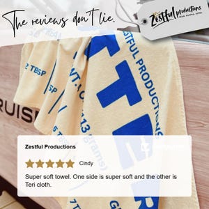 May include: Cream-coloured towel with large blue block letters and the text "Zestful Productions". The towel has the text "The reviews don't lie" in cursive. A customer review is also visible.