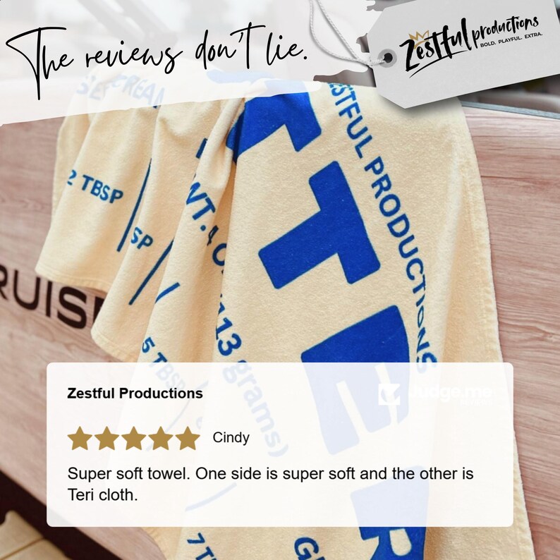 May include: Cream-coloured towel with large blue block letters and the text "Zestful Productions". The towel has the text "The reviews don't lie" in cursive. A customer review is also visible.
