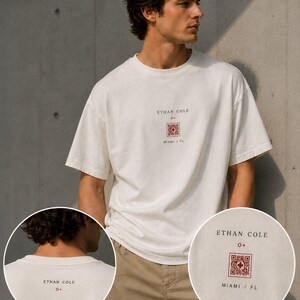 May include: Cream-colored t-shirt with the text "ETHAN COLE" and a red and white graphic. The shirt has a relaxed fit and short sleeves. The text "MIAMI / FL" is below the graphic.