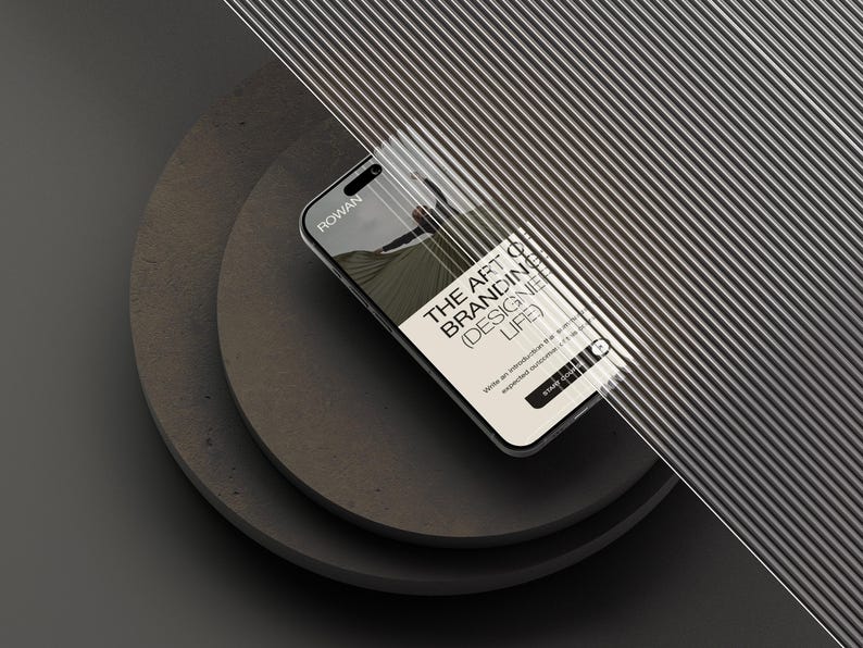 May include: A smartphone displaying a screen with the text ROWAN, THE ART OF BRANDING (DESIGNER LIFE), and START COURSE, partially obscured by a ribbed glass panel, resting on two stacked dark gray circular platforms against a dark background.