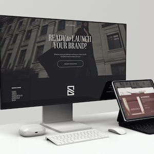 May include: A modern workspace setup featuring a large computer monitor displaying a website with the text "READY TO LAUNCH YOUR BRAND?" and a tablet with a keyboard. A white keyboard, mouse, and wireless earbuds are also on the desk.