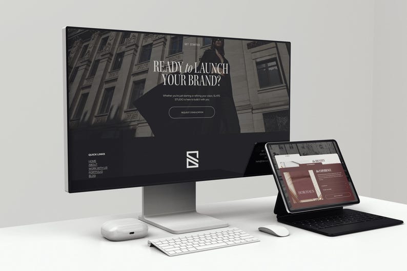May include: A modern workspace setup featuring a large computer monitor displaying a website with the text "READY TO LAUNCH YOUR BRAND?" and a tablet with a keyboard. A white keyboard, mouse, and wireless earbuds are also on the desk.