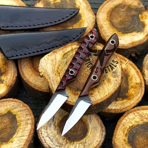 K&ouml;nnte beinhalten: Zwei feststehende Messer mit silbernen Stahlklingen und Holzgriffen. Ein Griff hat eine texturierte, dunkelrote Oberfl&auml;che, w&auml;hrend der andere aus glattem, dunkelbraunem Holz besteht. Beide haben Messingnieten und zwei schwarze Lederscheiden.
