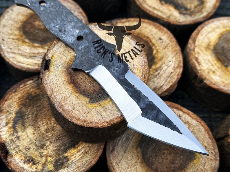 May include: A black and silver knife with a partially polished blade. The knife is resting on a stack of wooden rounds. The text "Rick's Metals" is visible on the knife.