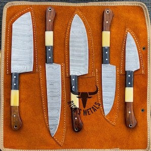 May include: A set of five knives with wooden handles and a patterned blade, displayed in a brown leather roll with the text "Rick's Metals".