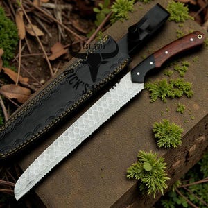Peut inclure: Un long couteau dentelé avec un manche en bois foncé et une lame décorative, posé à côté d'un étui en cuir noir. L'étui est gaufré d'un motif et du texte "RICK'S". Le couteau est sur une surface marron avec des plantes vertes.