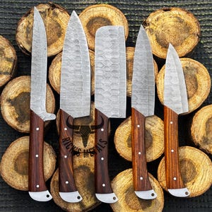 Peut inclure: Six couteaux de cuisine avec des manches en bois et une finition martel&eacute;e. Les couteaux sont dispos&eacute;s sur un fond de rondins de bois. Le texte "Rick's Metals" est visible sur les lames.
