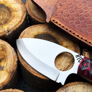 May include: A silver knife with a black and red handle. The knife has a finger hole in the handle and the words "Rick's Metal" are visible on the handle.