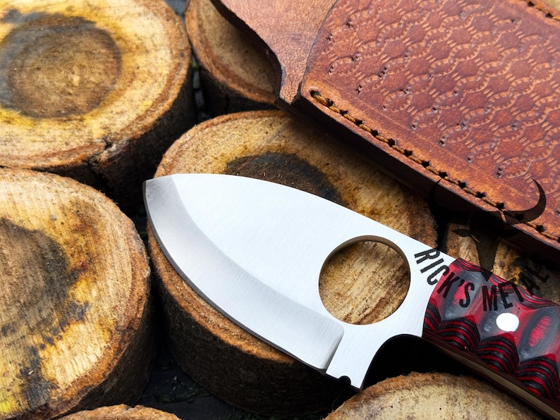 May include: A silver knife with a black and red handle. The knife has a finger hole in the handle and the words "Rick's Metal" are visible on the handle.