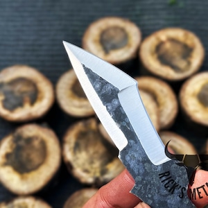 May include: A close-up of a small, black and silver knife with a unique, angular blade. The knife has a textured, hammered finish and the text "Rick's Metals" is engraved on the handle.