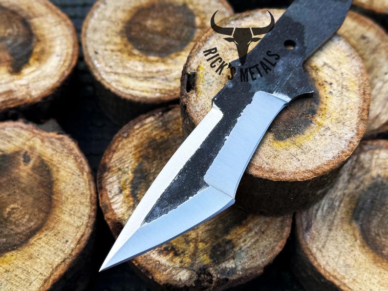 May include: A black and silver knife with a sharp point and a curved blade. The knife is resting on a stack of wooden rounds.