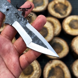 May include: A close-up of a hand holding a small, silver knife with a black handle. The knife has a sharp point and a slightly curved blade. The knife is labeled "Rick's Metals".