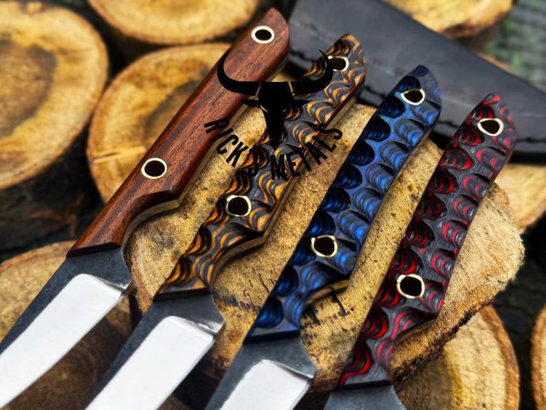 May include: Close-up of four custom knives with various handle designs. The handles feature wood grain, and patterned resin in shades of brown, blue, and red. Each knife has a silver blade and brass accents. The knives are displayed on a wooden surface.