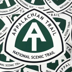 May include: White and green Appalachian Trail National Scenic Trail stickers. The stickers feature a white "A" within a green triangle, surrounded by the text "APPALACHIAN TRAIL" and "NATIONAL SCENIC TRAIL" in black.
